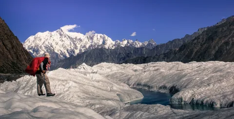Senderista de pie sobre cumbre glaciar, panorámica de cordillera al fondo